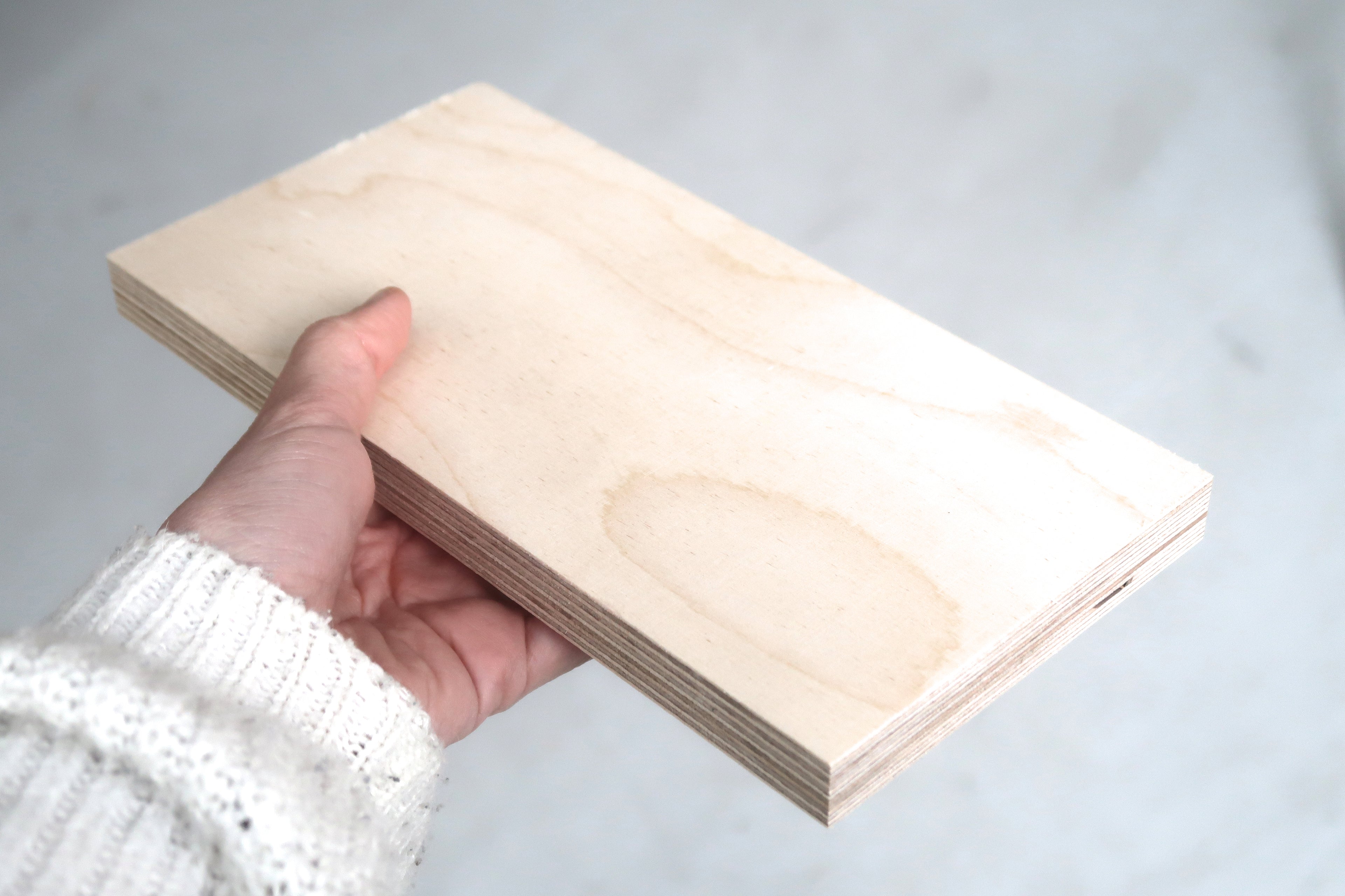 Hand holding a stylish modular wooden pegboard shelf panel with a smooth natural finish.