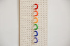 Red, orange, yellow, green, blue and purple coloured rings lined up on a birch pegboard