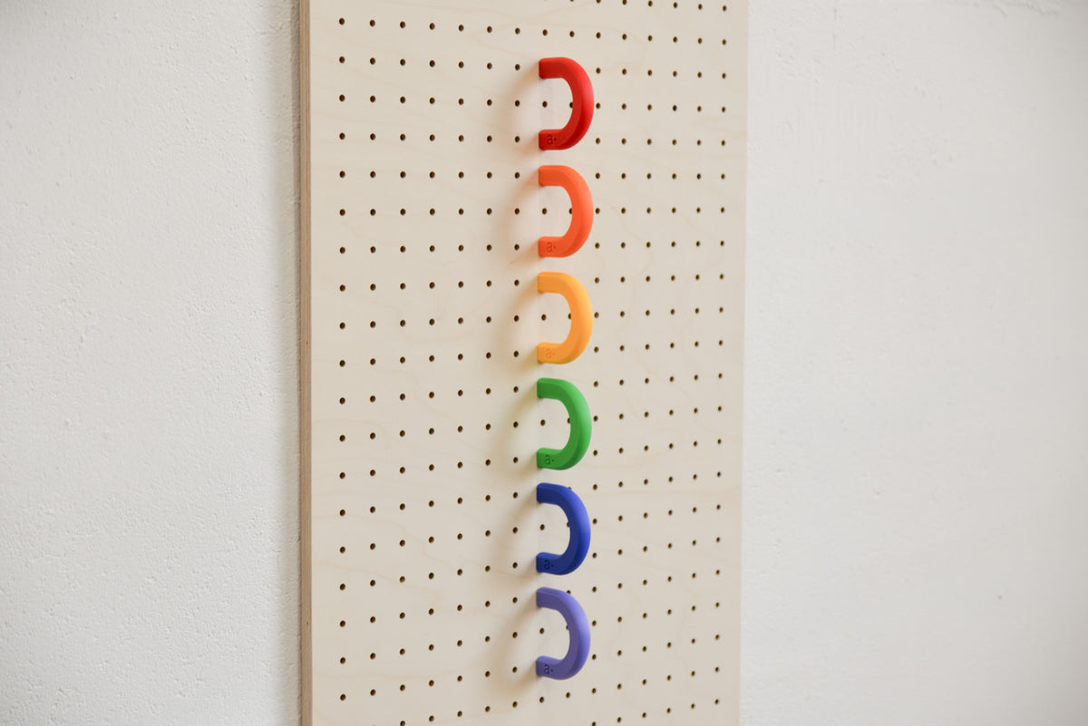 Red, orange, yellow, green, blue and purple coloured rings lined up on a birch pegboard