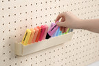 Hand pakt een pastelkleurige markeerstift uit de kantelbare pegboardhouder - Aire