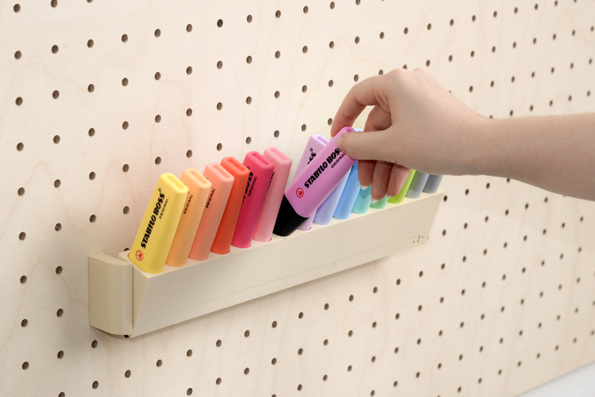Hand pakt een pastelkleurige markeerstift uit de kantelbare pegboardhouder - Aire