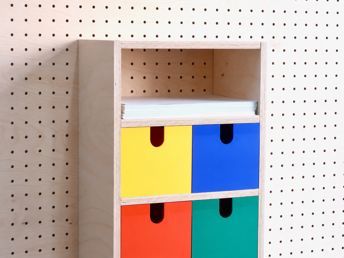 Detail van de opbergbox met 3 vakken: gekleurde lades en een pak A4-papier aan een houten pegboard